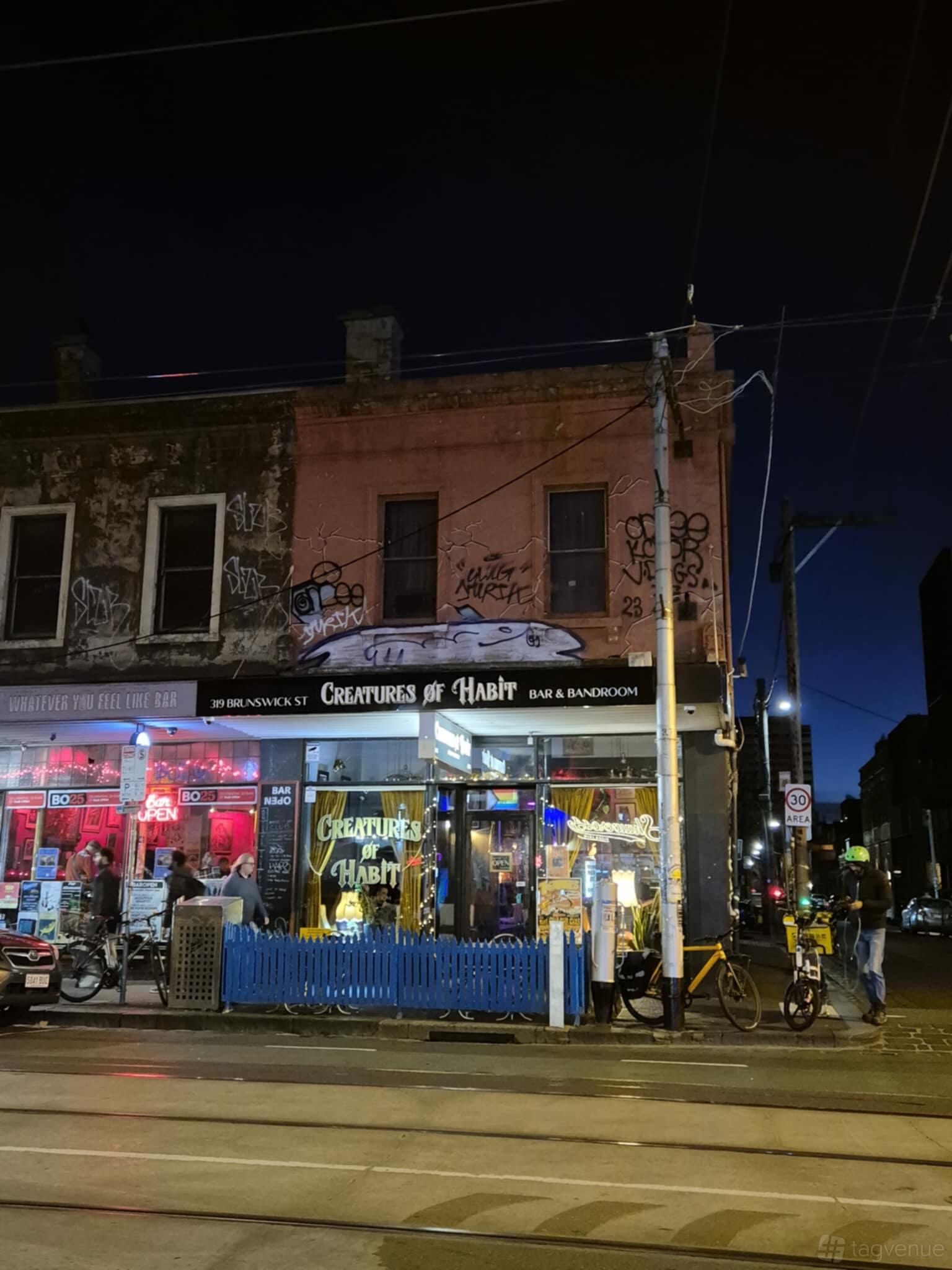 A pub with a neon sign, street-facing entrance, and exterior graffiti at Creatures of Habit Bar & Bandroom.