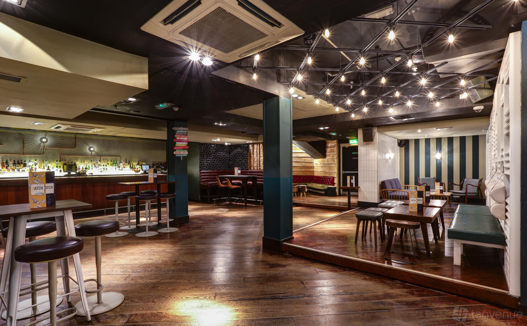 An event space in a cocktail bar with wooden floors, exposed bulbs on the ceiling, and a long bar at Patch St Paul's.