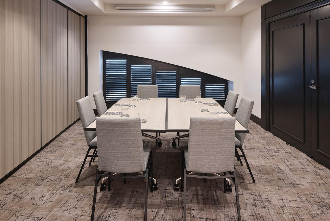 An event space with a long conference table, eight cushioned chairs, and patterned carpet at Rydges Darling Square.