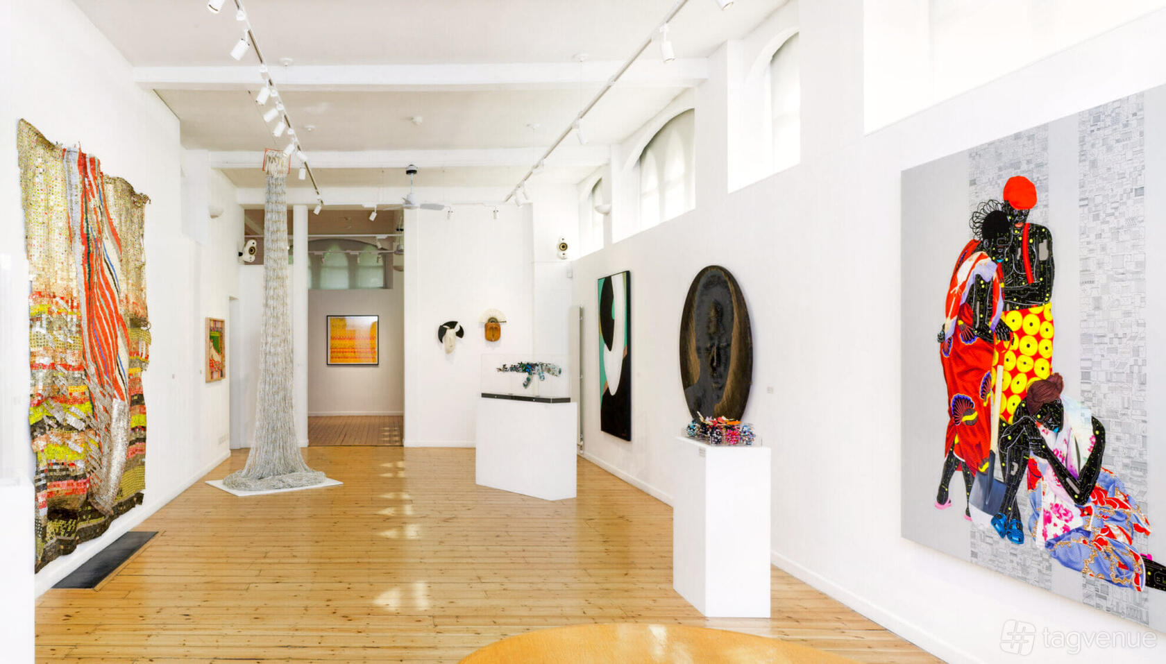 A gallery with high ceilings, wood floors, white walls, and contemporary artwork displays at October Gallery.