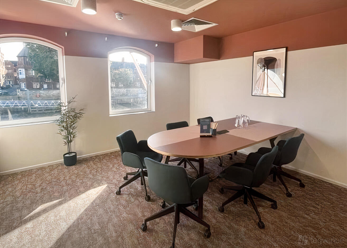 A meeting room with arched windows, a long oval table, rolling chairs, and natural light at Wizu Workspace - East Coast House.