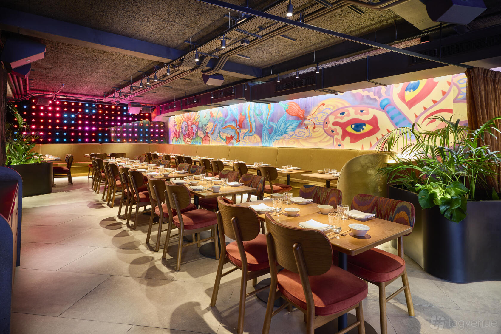 A restaurant lounge with colorful mural walls, rows of wooden tables, and cushioned chairs at Chotto Matte.