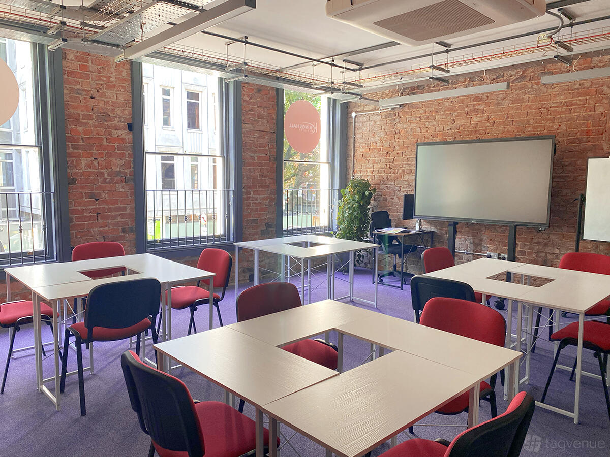 A classroom with exposed brick walls, large windows, red chairs, and modular desks at Kings Hall College.