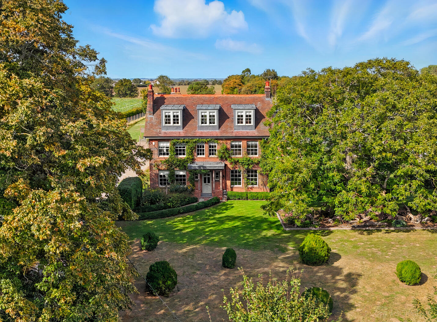 A country house with red brick exterior, tall chimneys, and large front lawn surrounded by mature trees at Thorpe Farm.