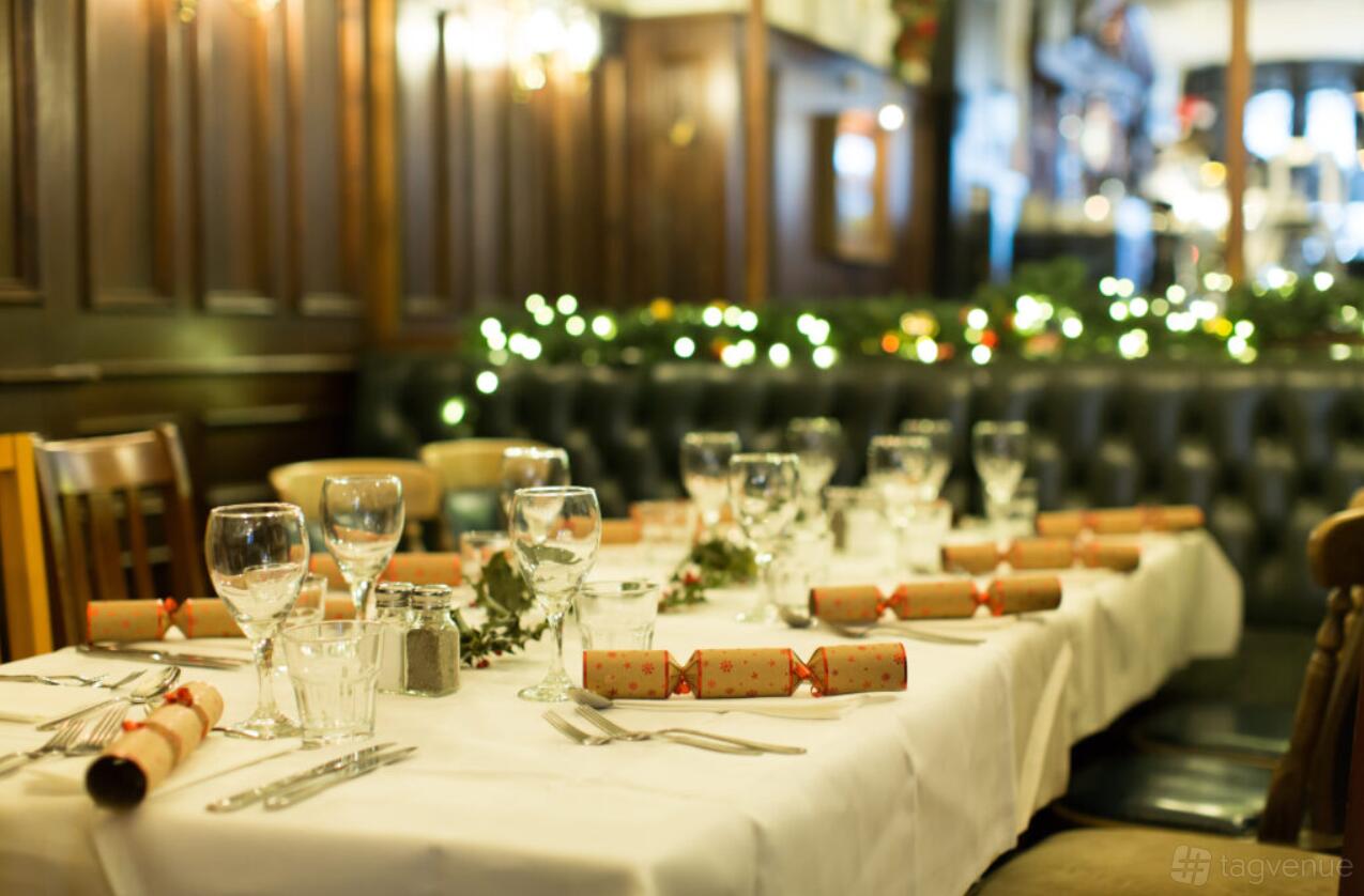 An event space with white-clothed tables, festive decorations, glassware, and dark wood paneling at Aviary Rooftop Bar & Restaurant.