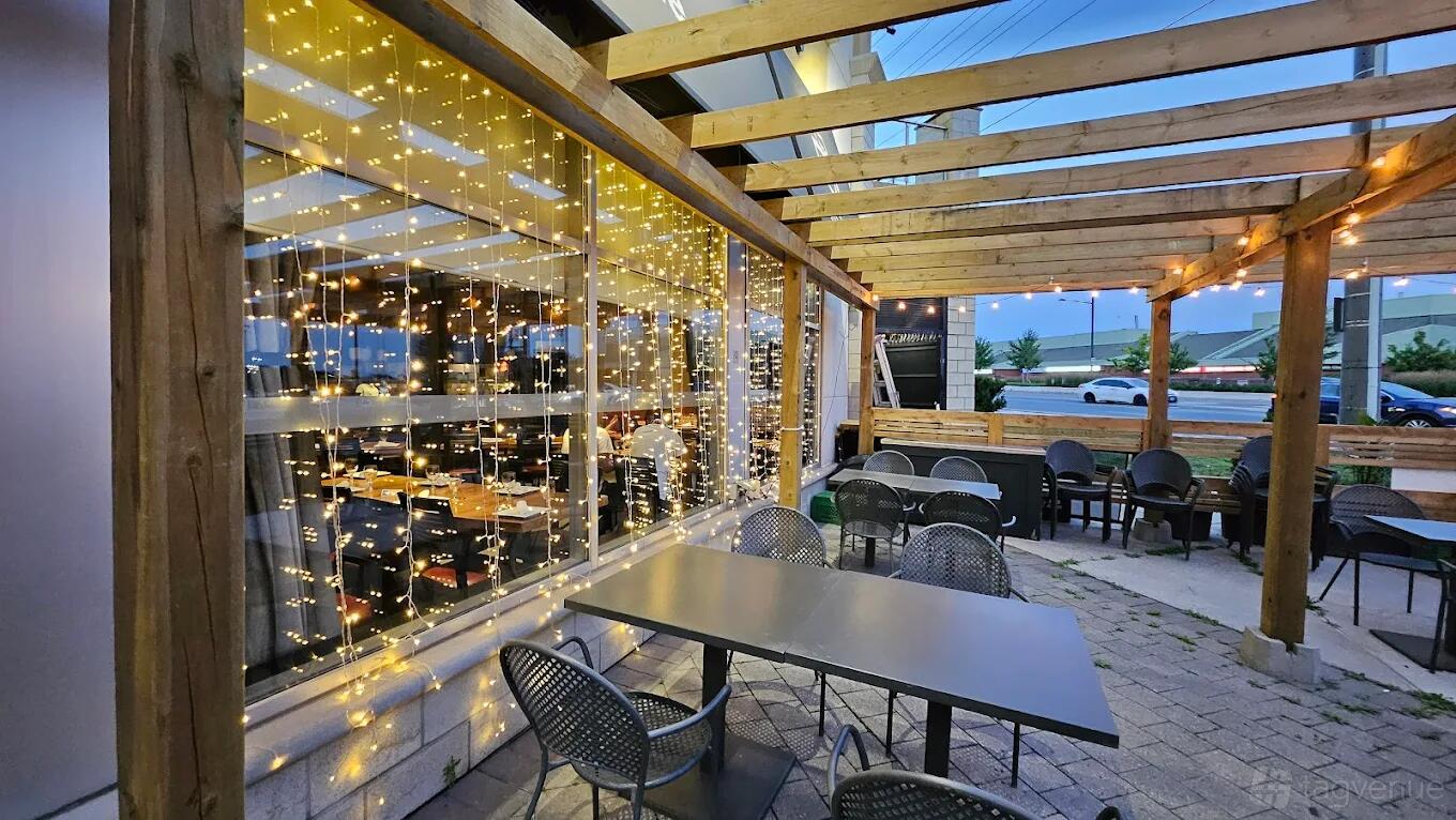 An outdoor restaurant patio with wooden pergola, string lights, and metal dining tables at Desi Pakwan.