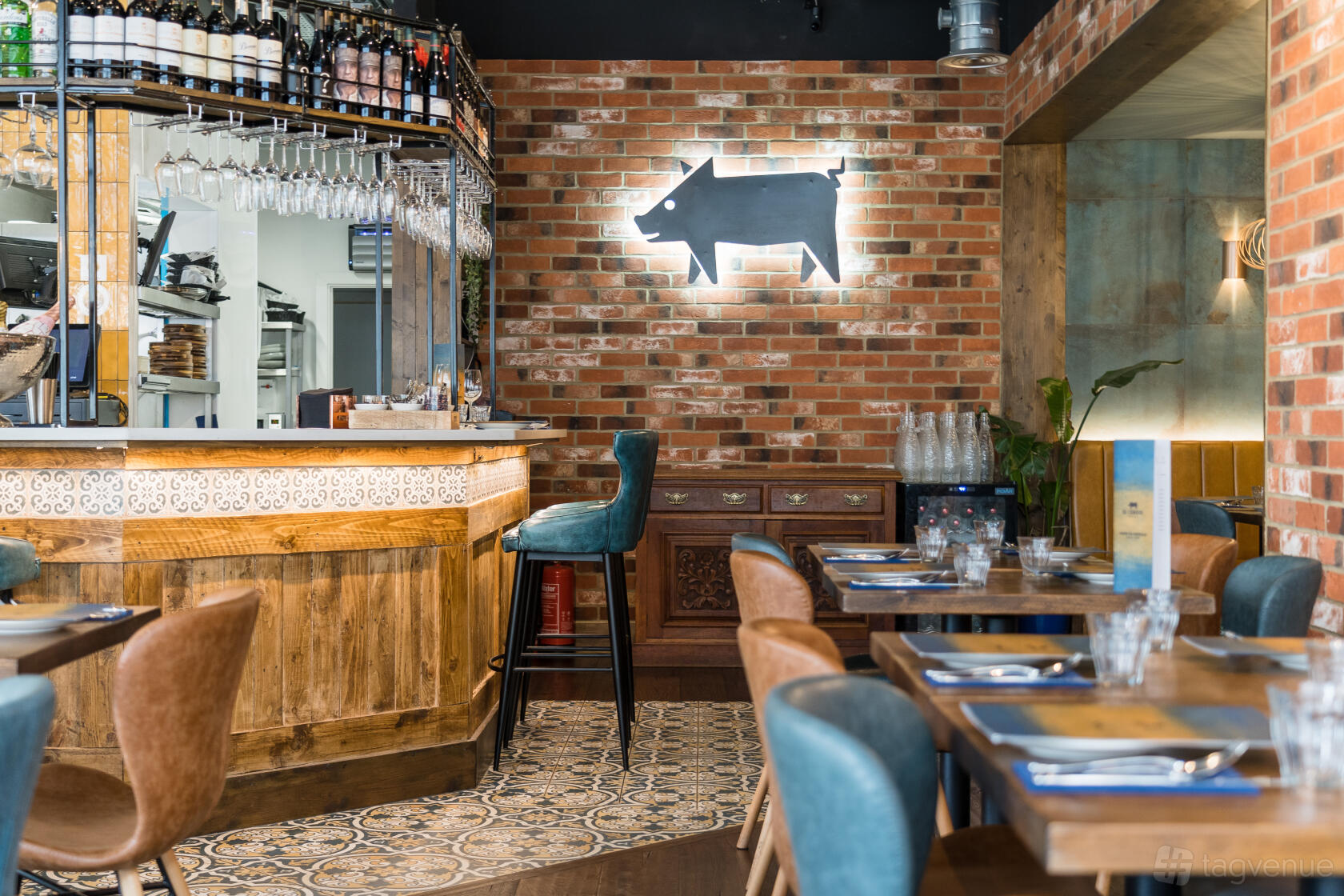 A restaurant with exposed brick walls, patterned tile flooring, a wooden bar, and a neon pig sign at El Cerdo Maidenhead.