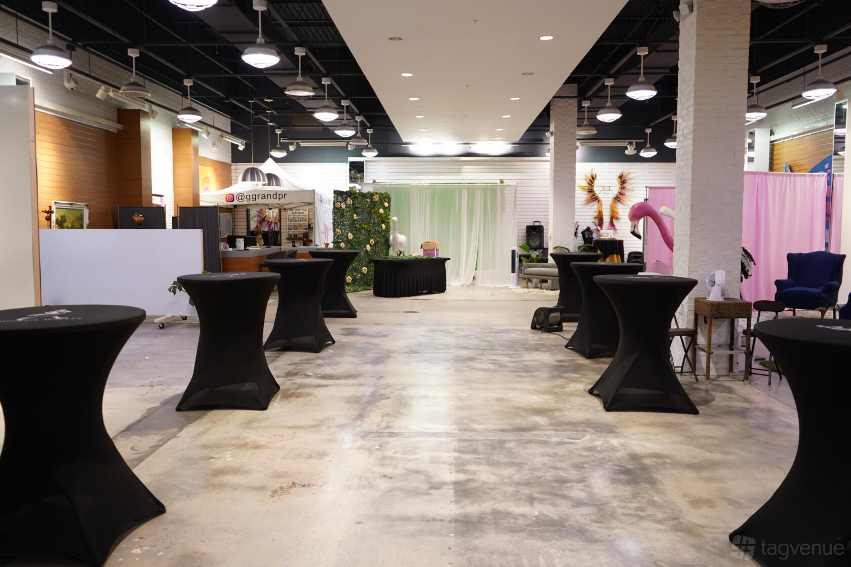 A creative space with high ceilings, concrete floors, round cocktail tables, and decorative backdrops at CAP Village.
