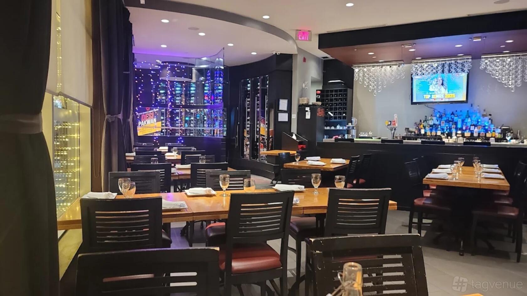 An event space in a restaurant with wooden tables, black chairs, string lights, and a glass wine display at Desi Pakwan.