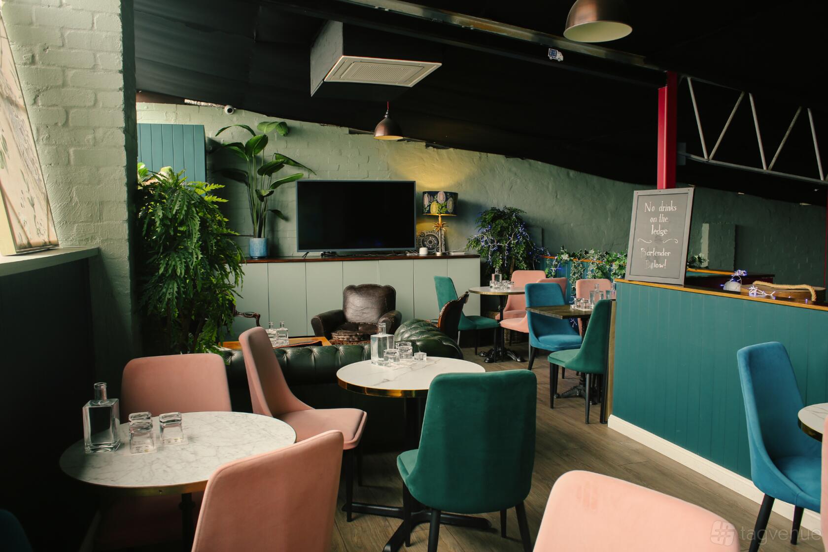 An event space in a bar with velvet chairs, marble tables, and large potted plants at Goodradigbee Distillers.