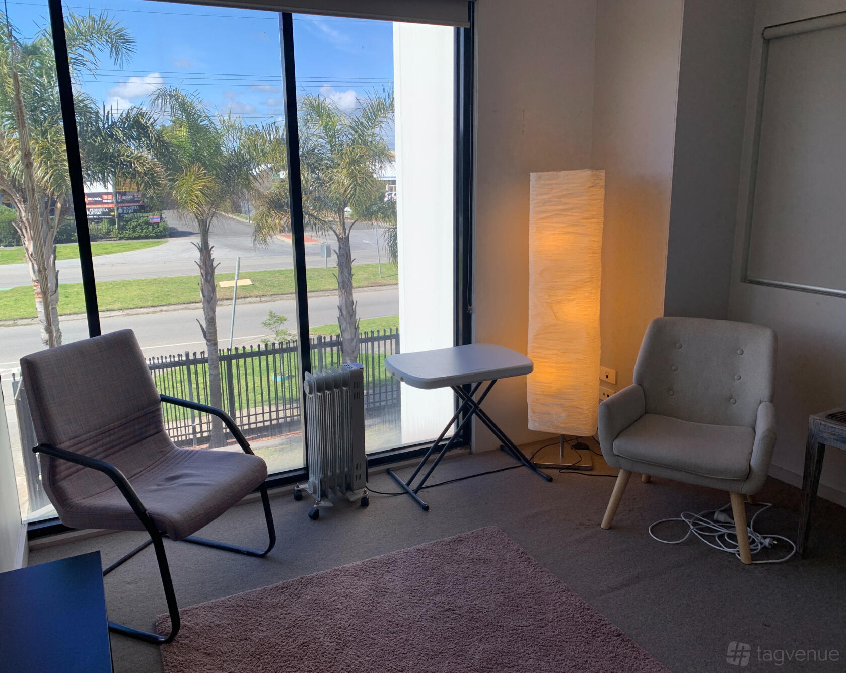 A therapy room with two armchairs, a small table, floor lamp, and large windows at Liefde Wellness Centre.