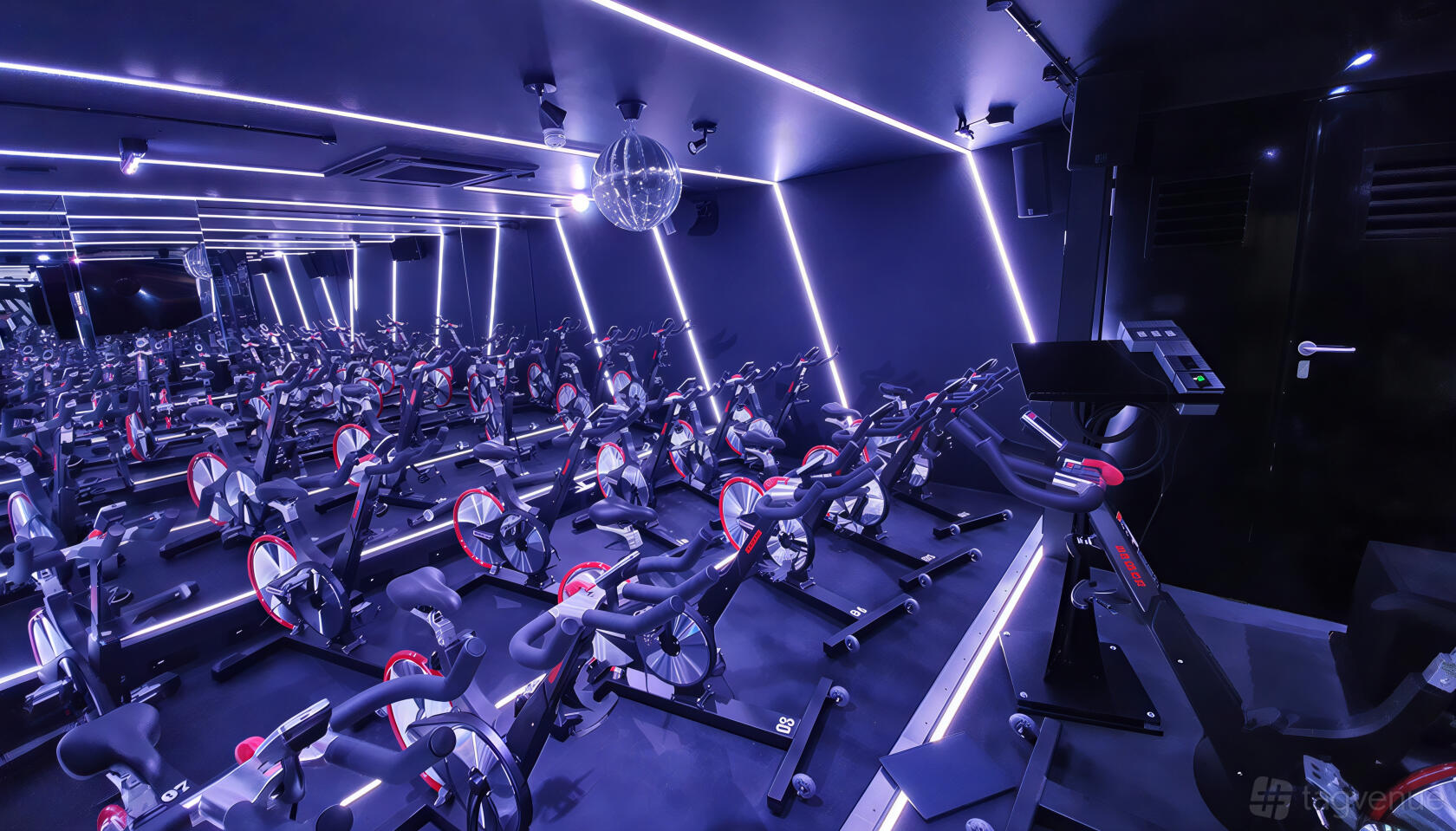 A spin studio with rows of stationary bikes, mirrored walls, LED strip lighting, and a disco ball at RUMBLE.