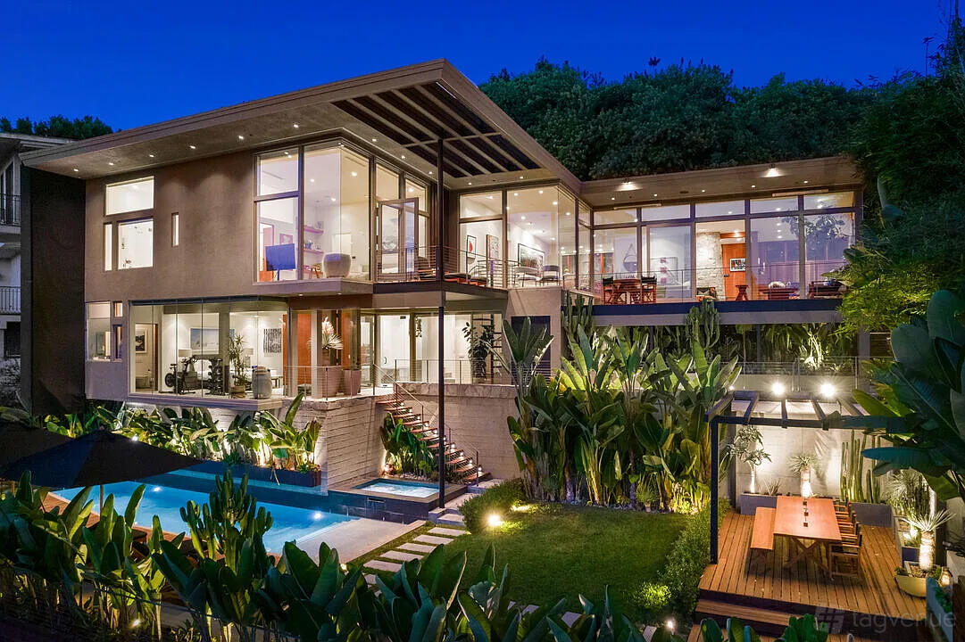 A house with floor-to-ceiling windows, a swimming pool, lush landscaping, and a wooden deck at The Waynecrest Two.