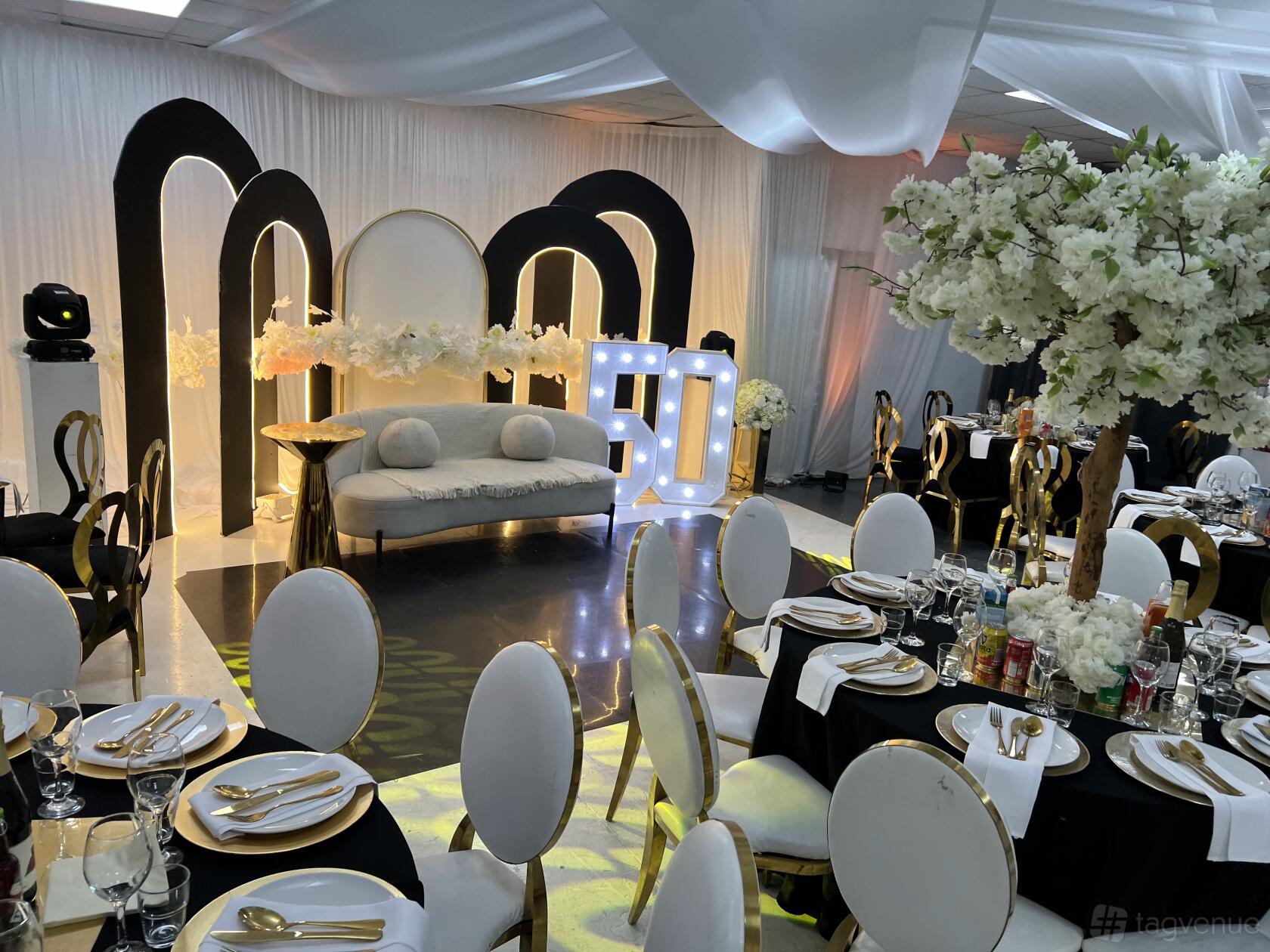 A creative space in a photo studio with draped white walls, round tables with black and white linens, and a decorative floral arch at KMP STUDIOS.
