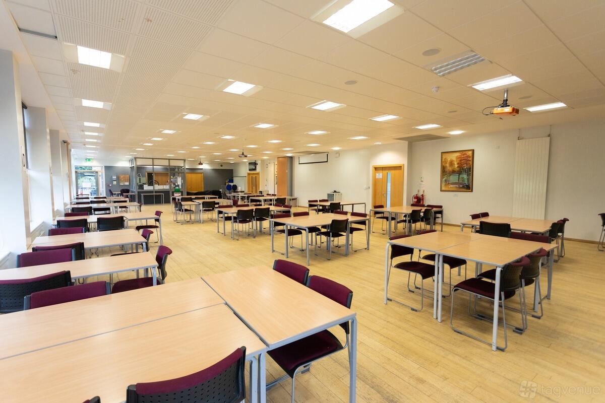 An event space with rectangular tables, stackable chairs, and wood flooring at King Edward VI Five Ways School.