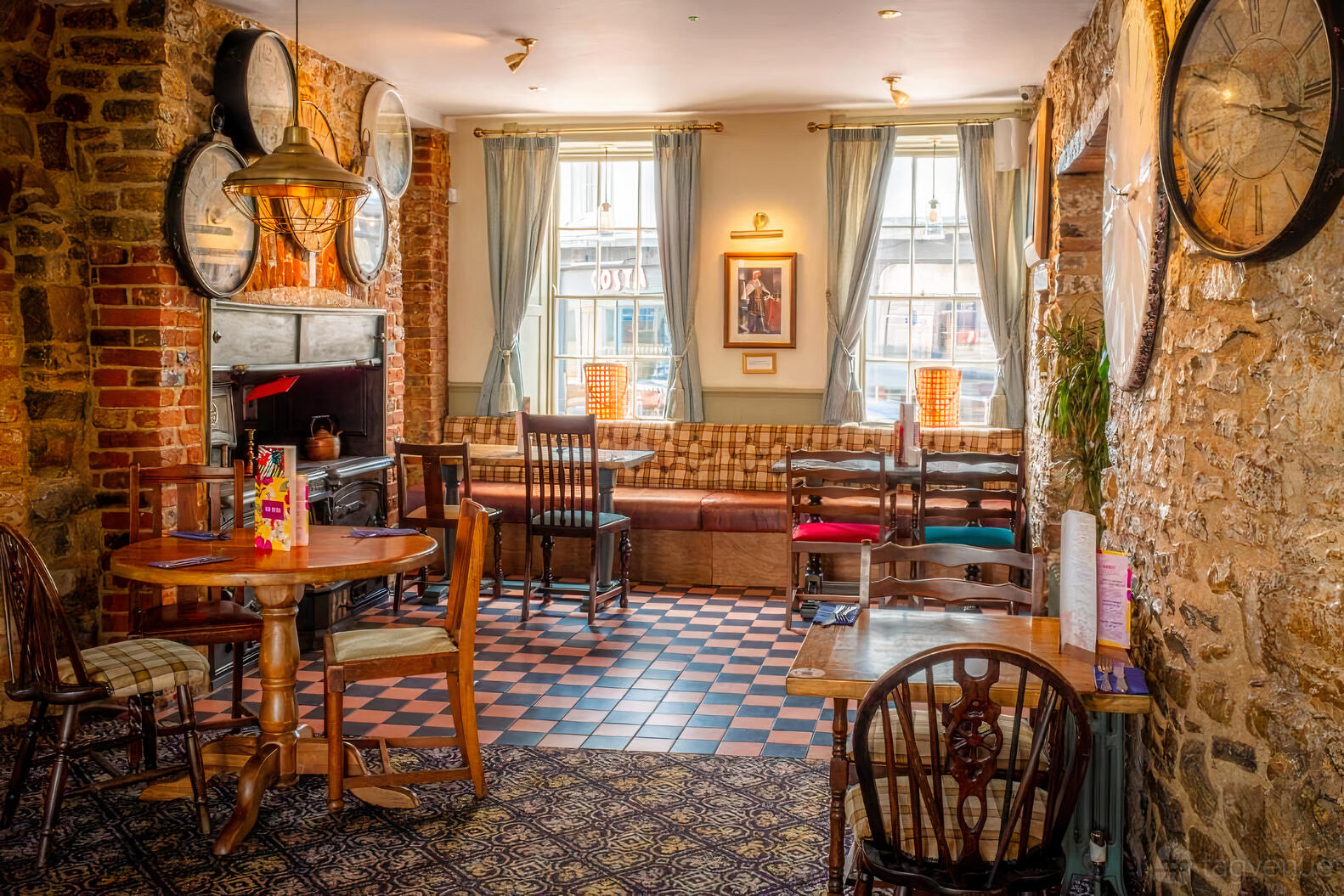 A function room in a hotel with exposed brick walls, large vintage clocks, and checkered tile flooring at The George Hotel.