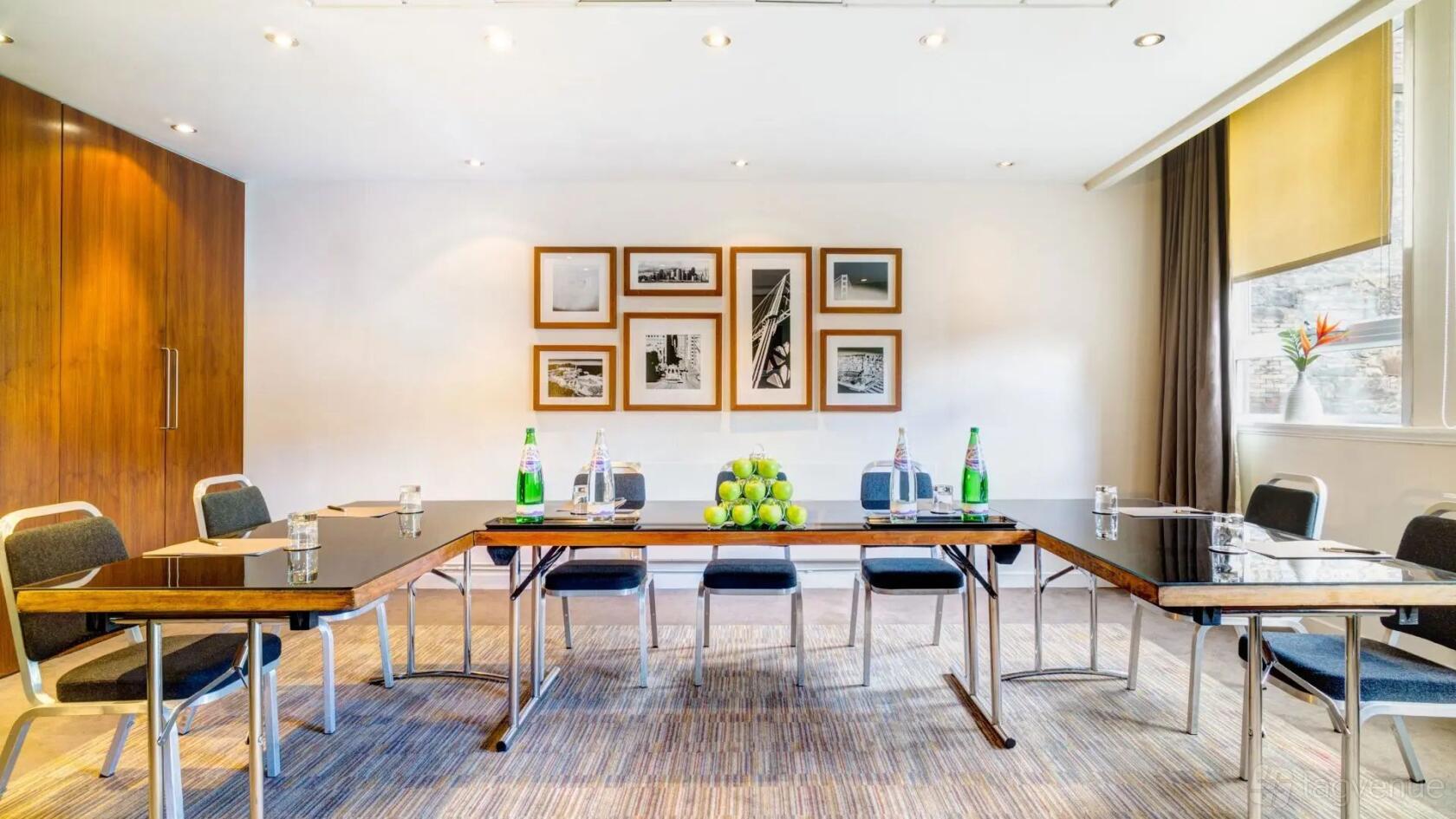 A meeting room with U-shaped tables, bottled water, green apples, and framed black-and-white photos at Apex Grassmarket Hotel.