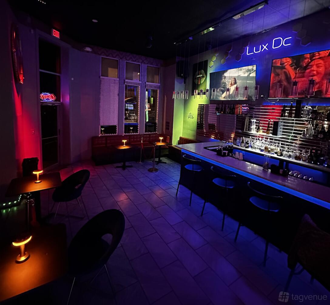 An event space in a bar with neon lighting, wall art, and a curved bar counter at Lux Dc Bar & Lounge.