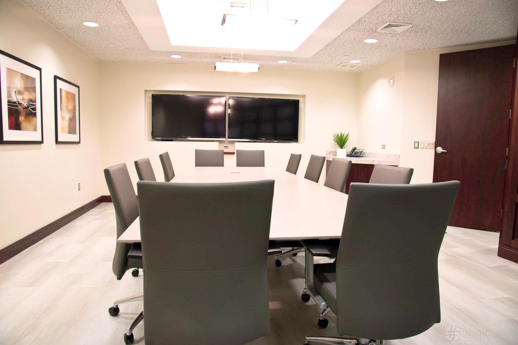 A boardroom with a long conference table, gray chairs, and dual wall-mounted screens at American Executive Centers - Malvern.