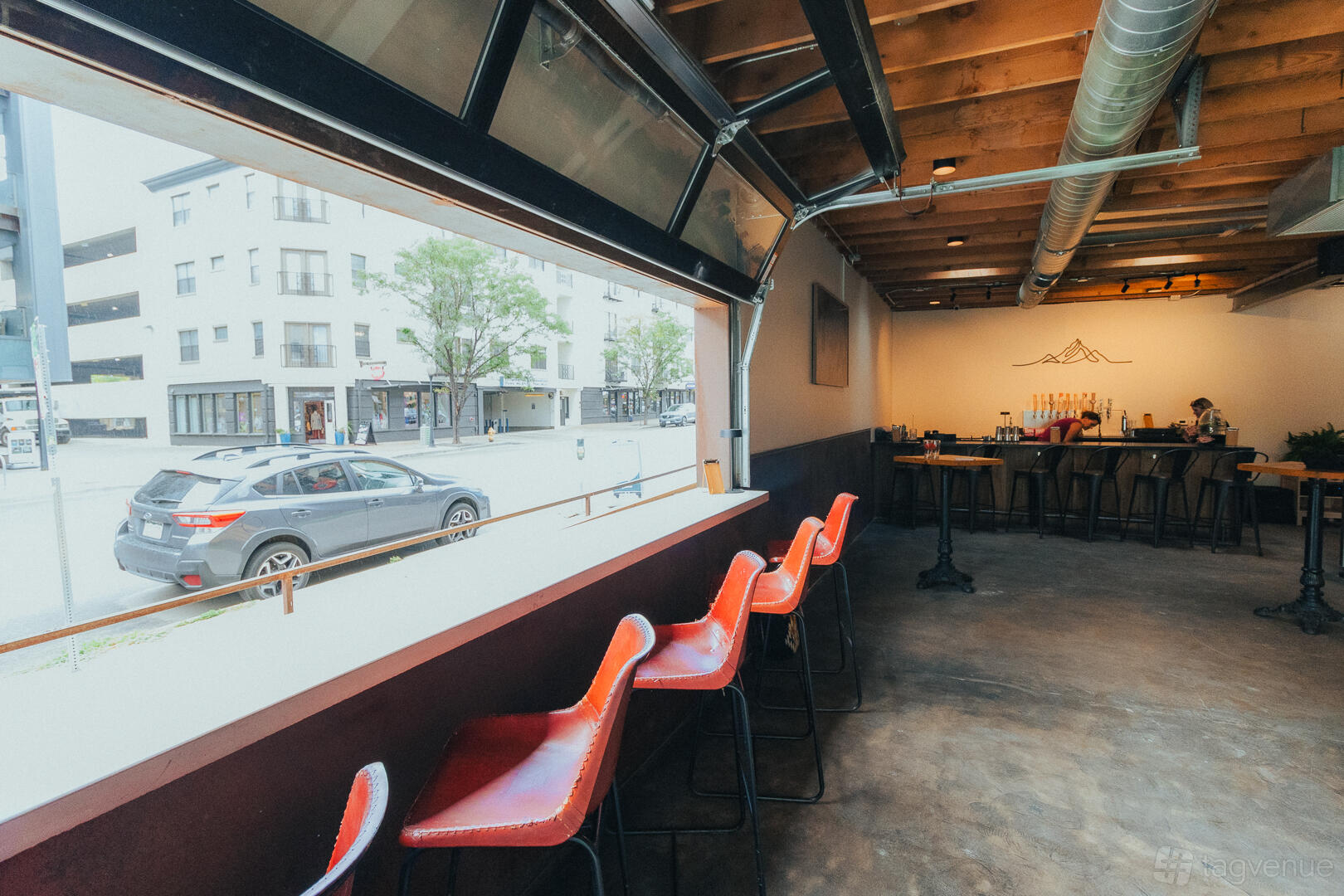 An event venue with red bar stools along a garage-door window, exposed ductwork, and a bar at The Outpost on Platte.