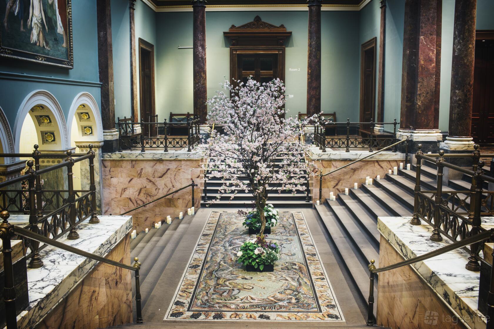 A museum terrace with a grand staircase, ornate mosaic floor, marble railings, and a blossoming tree at The National Gallery.