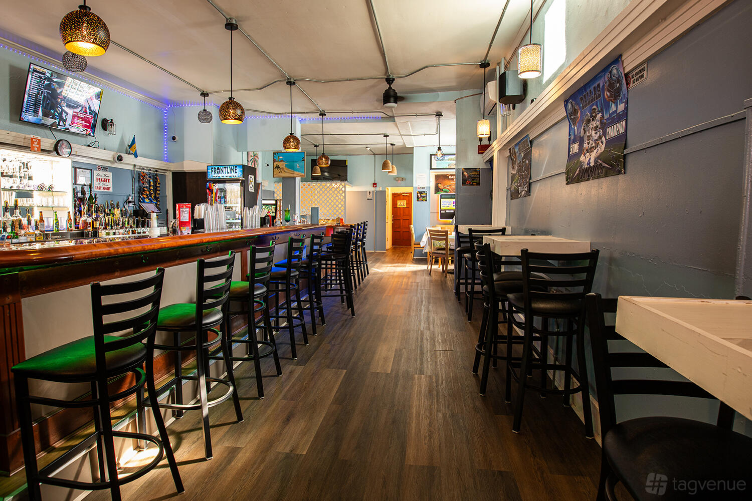 An event space in a bar with a long wooden counter, high stools, wall art, and pendant lighting at Frontline Island Bar and Grill.