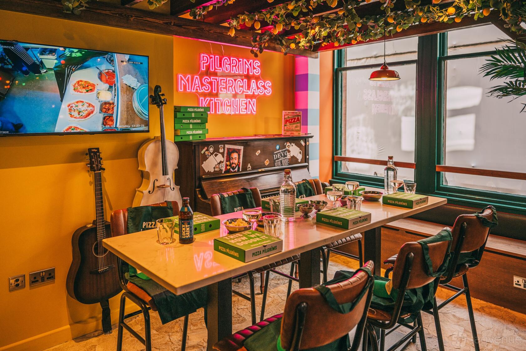 A restaurant dining space with a communal table, pizza boxes, neon sign, and musical instruments at Pizza Pilgrims Edinburgh.