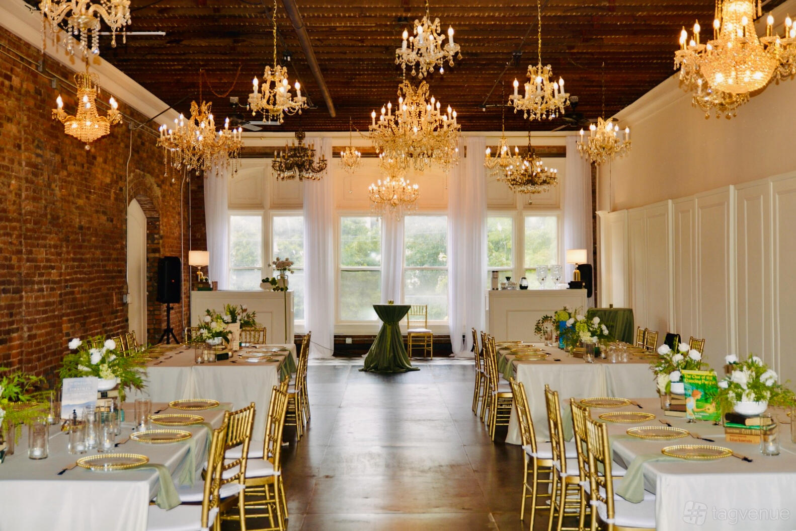 An event venue with exposed brick walls, crystal chandeliers, gold chairs, and large windows at theBindery.
