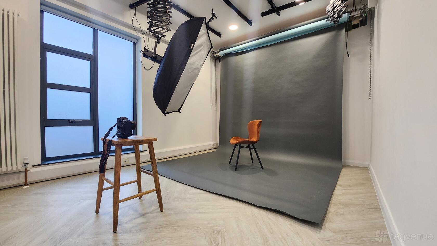 A photo studio with a seamless grey backdrop, studio lighting, and a single chair at Whitehall Studios.