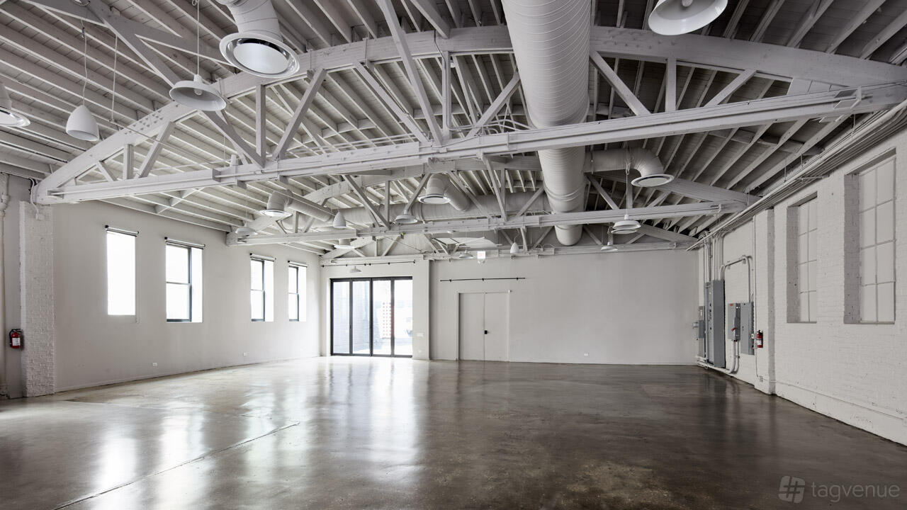 A photo studio with polished concrete floors, exposed white ceiling beams, and large windows at Parchment Studios.