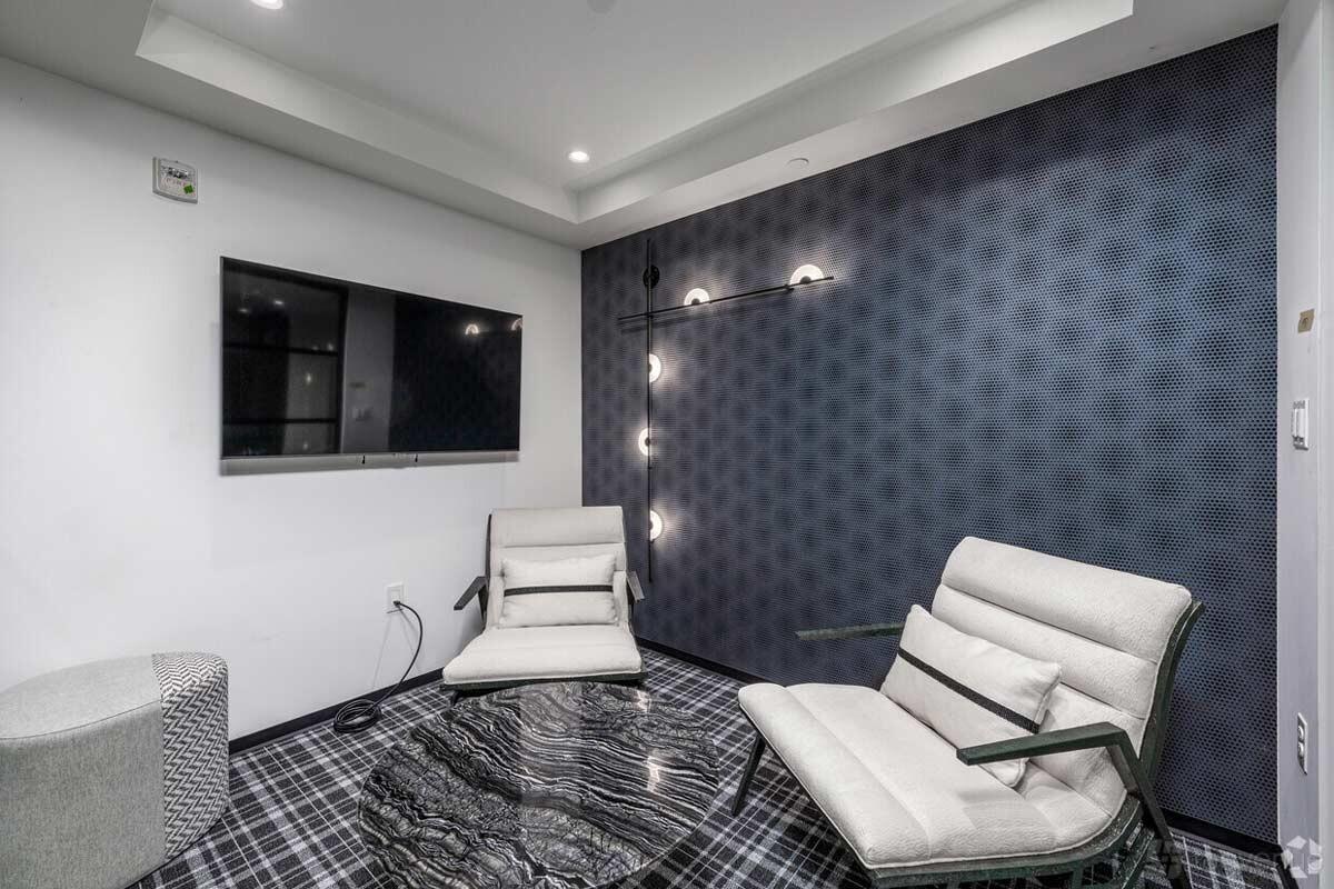 A meeting room with patterned carpet, modern armchairs, a marble oval table, and wall-mounted TV at Venture X Washington DC - Adams Morgan.