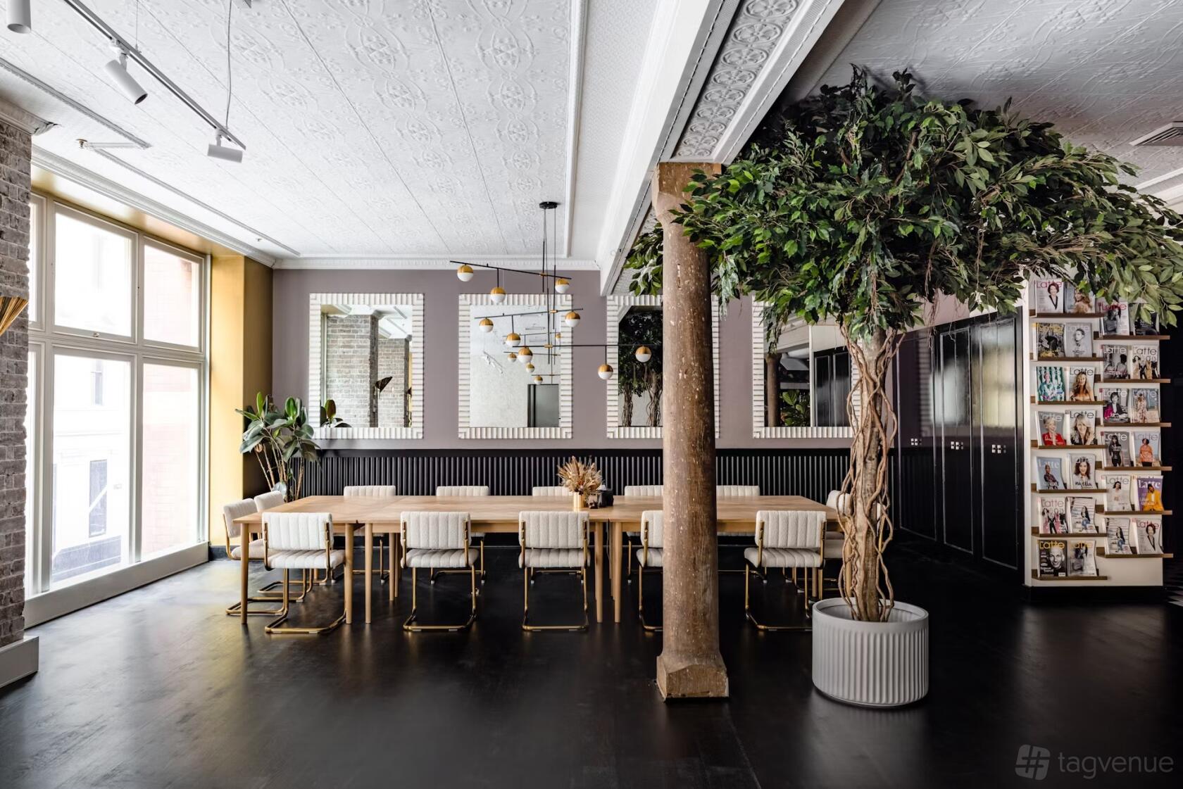 A meeting room with large windows, a long wooden table, white chairs, potted trees, and mirrored walls at Business Chicks.