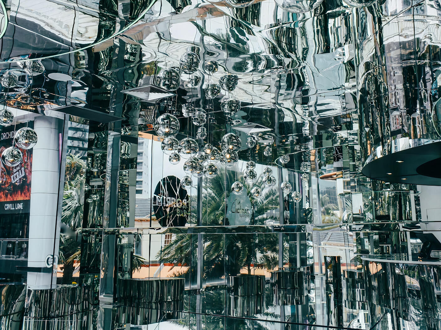 A bar with mirrored walls and ceiling, hanging metallic orbs, and reflections throughout at Mirror Bar.