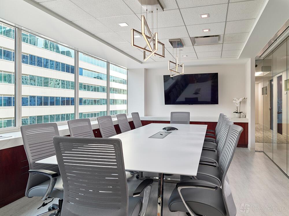 A boardroom with a long white conference table, ergonomic chairs, large wall-mounted screen, and floor-to-ceiling windows at American Executive Centers - Philadelphia.