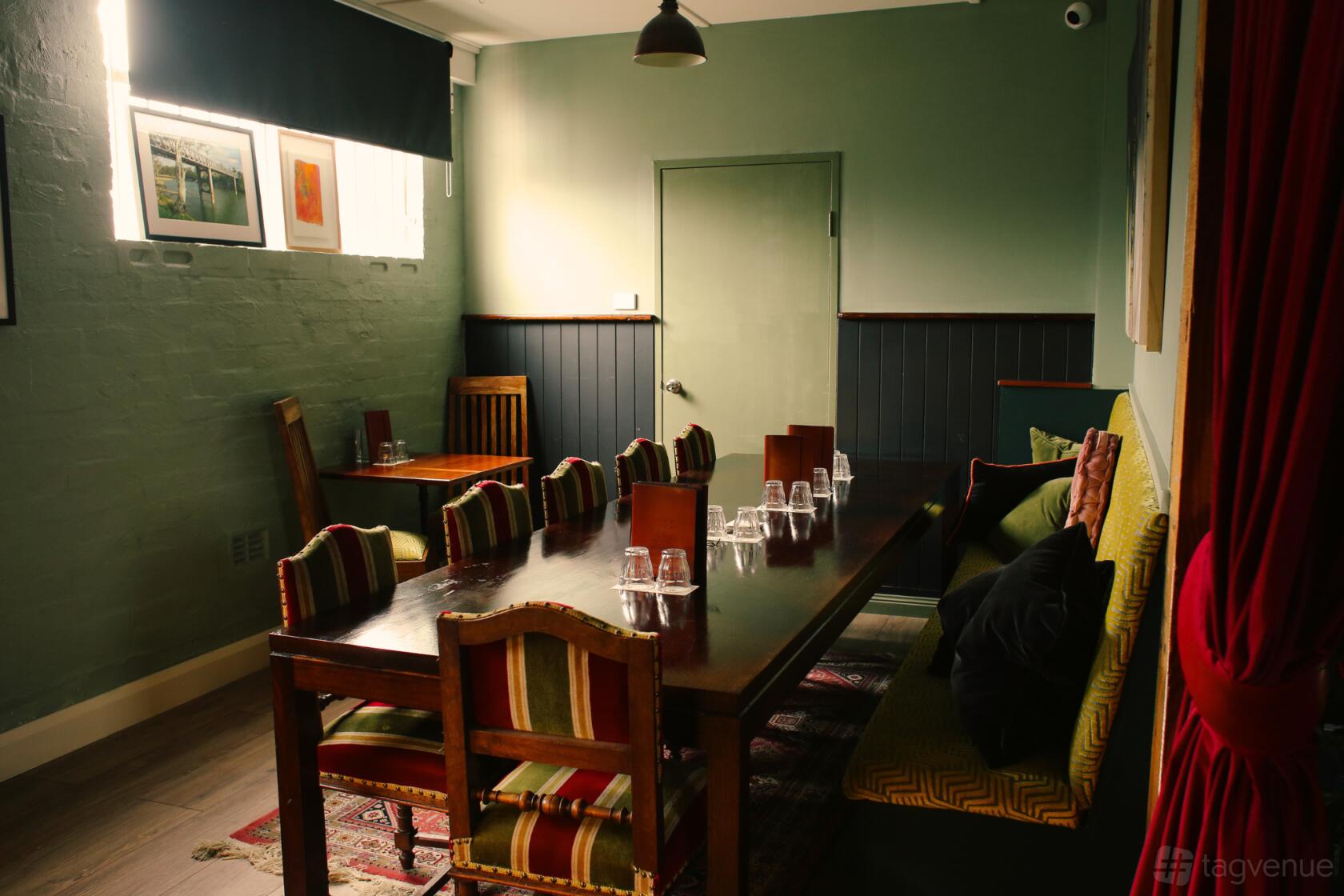 An event space in a bar with a long wooden table, striped chairs, cushioned bench seating, and framed art at Goodradigbee Distillers.