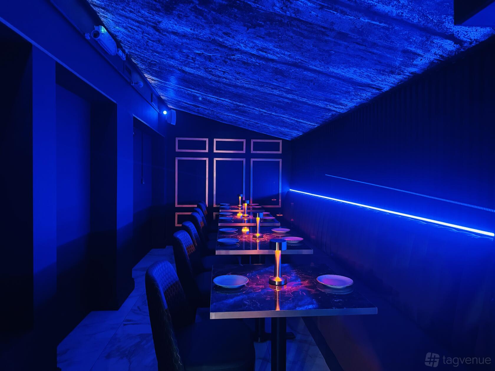 A restaurant with blue neon lighting, marble tables, and an exposed ceiling at Sapphire Dining.