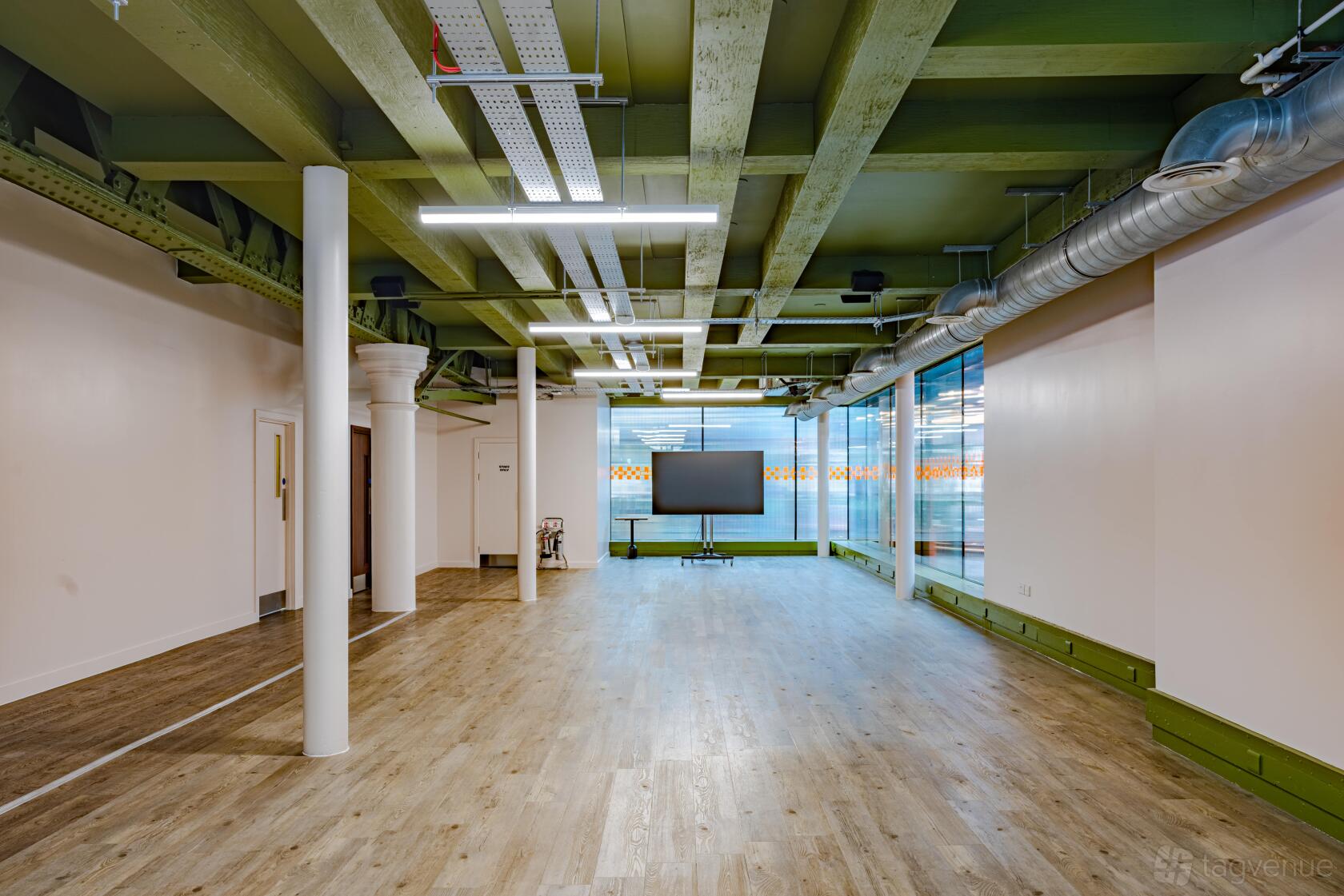 An event space with exposed ceiling beams, wood flooring, and floor-to-ceiling windows at KERB Social Club Spitalfields.