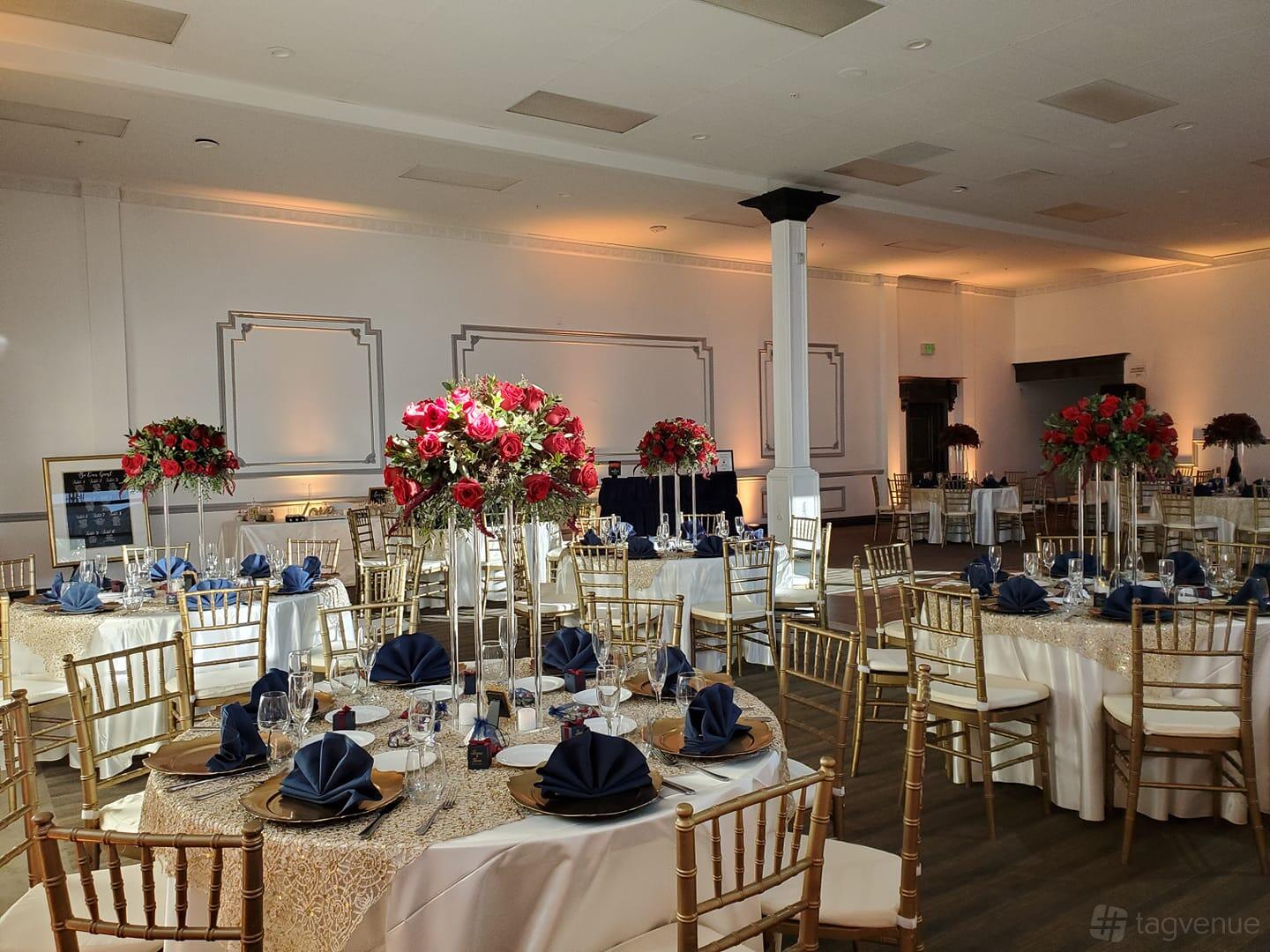 A banquet hall with round tables draped in patterned linens, gold chairs, and tall floral centerpieces at The Grand Theater.