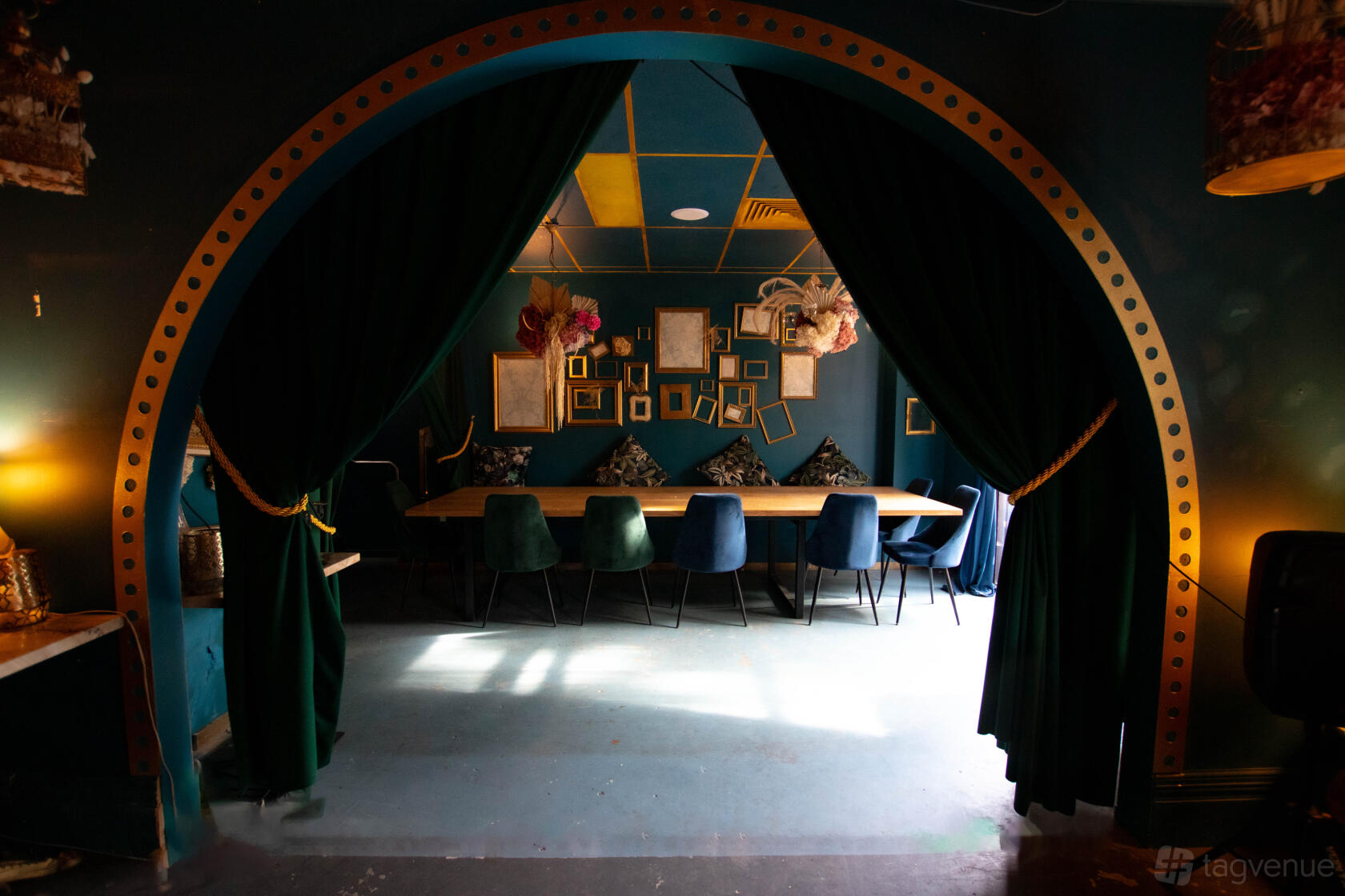 A dining room with velvet drapes, a long wooden table, mismatched chairs, and gold picture frames at Aces Bar @ Brunswick Aces.