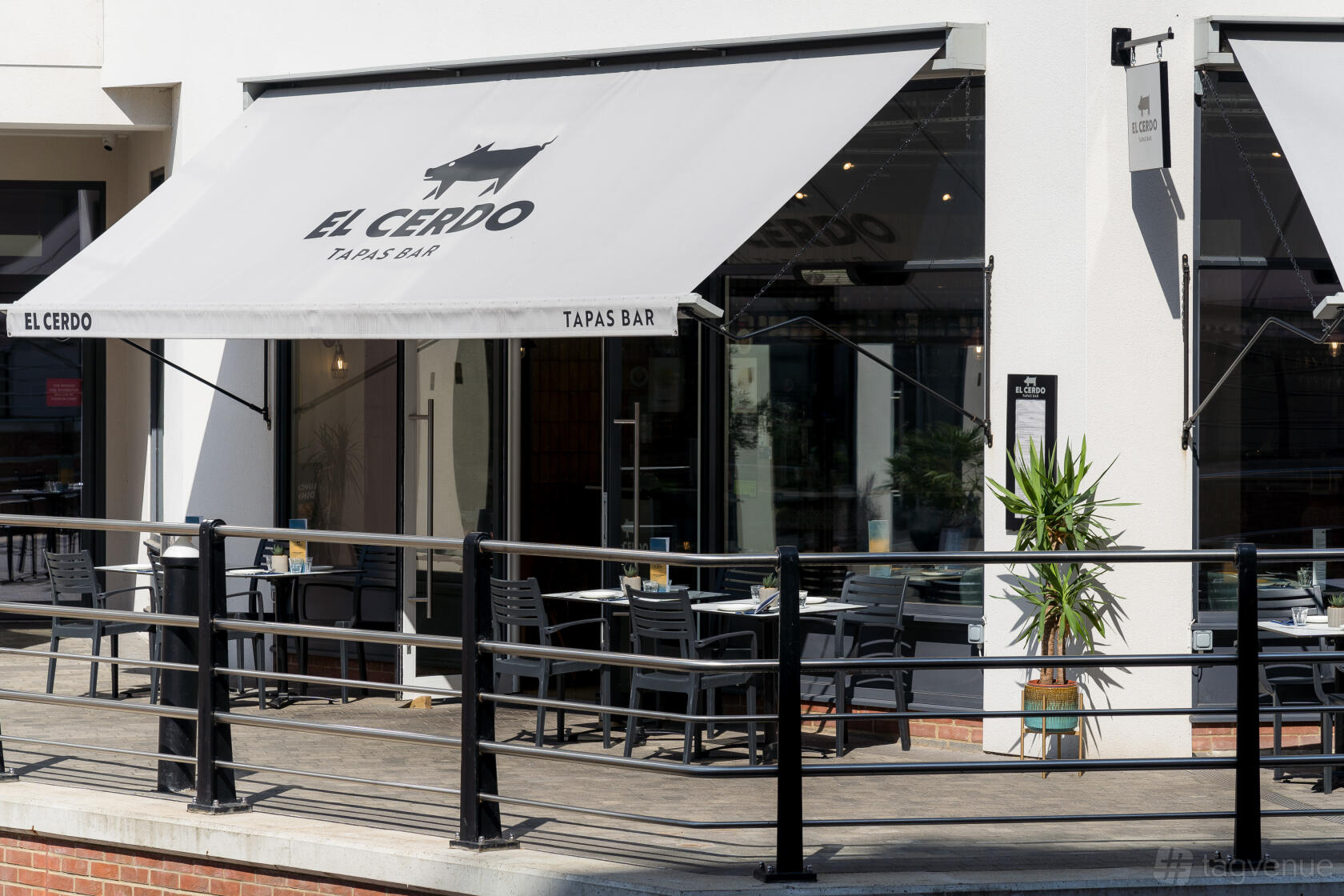 A restaurant with outdoor patio seating, black chairs, and large awnings at El Cerdo Maidenhead.