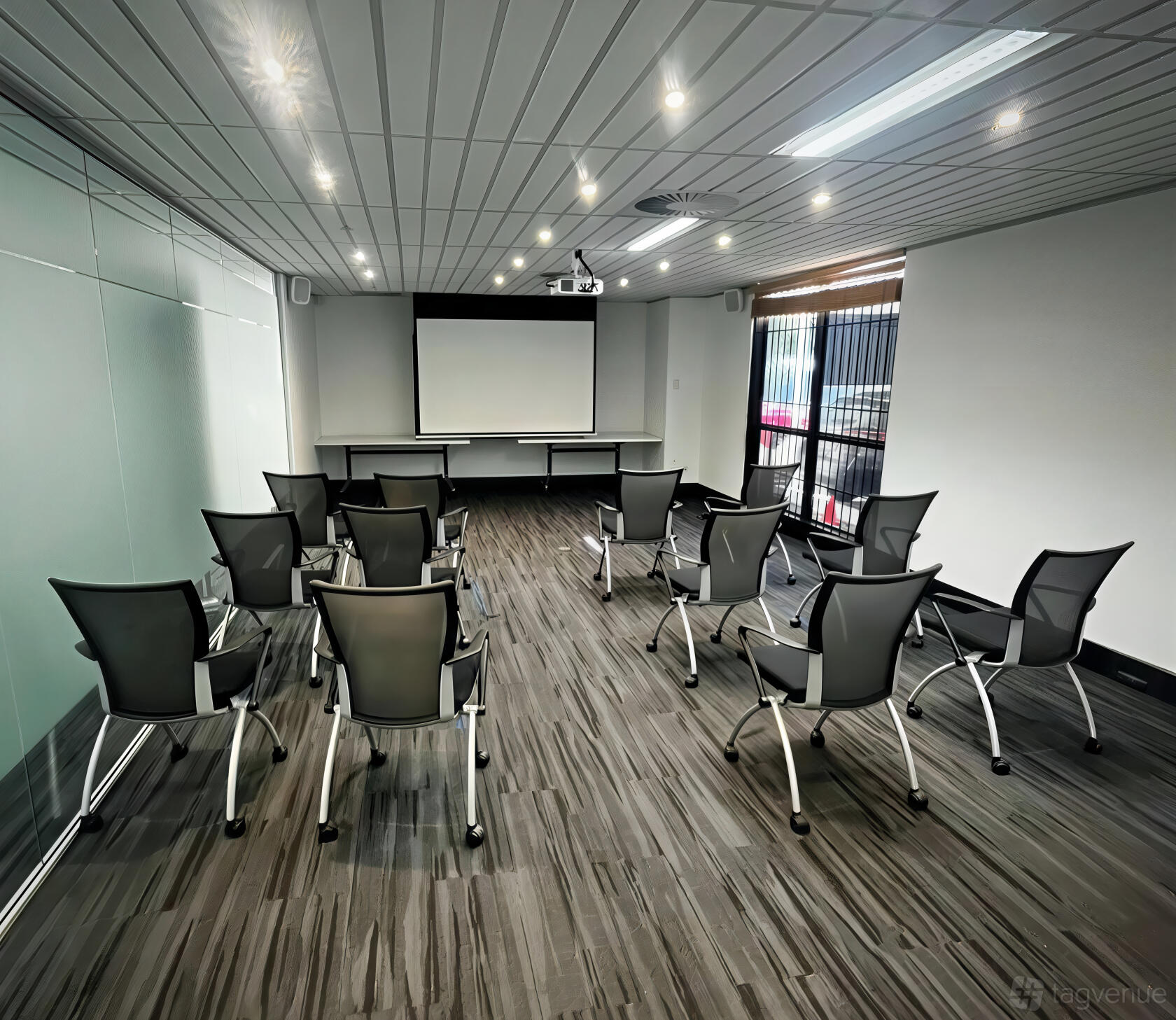 A boardroom with rows of black chairs, wood-grain flooring, and a projector screen at Optimum Health Solutions.