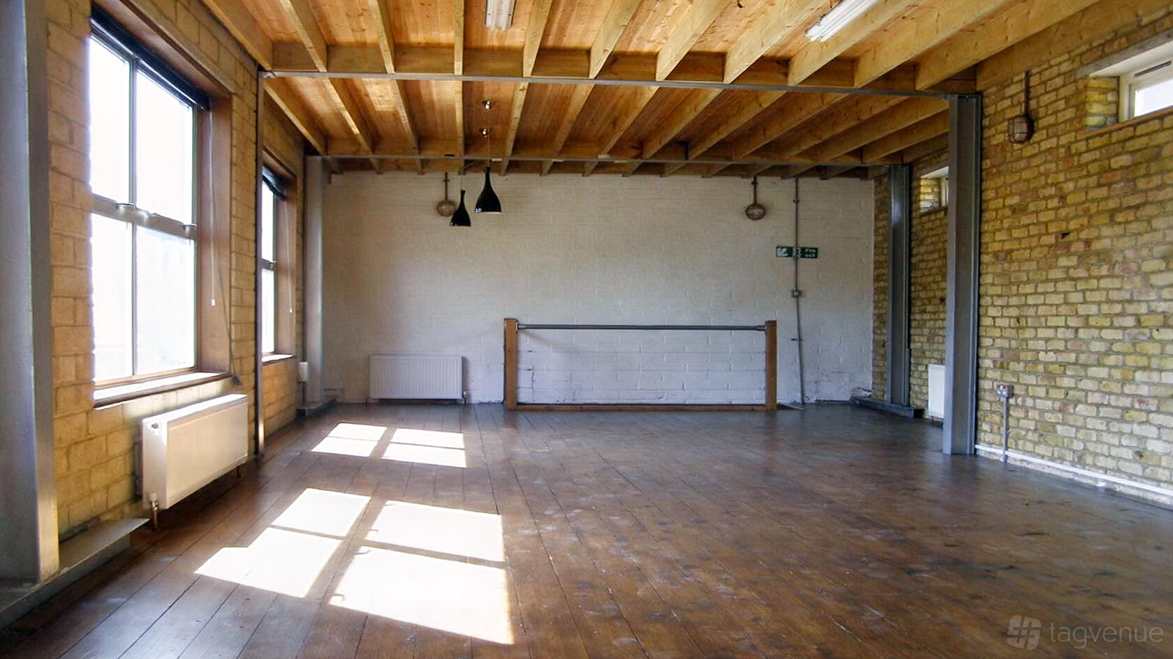 A rehearsal studio with exposed brick walls, wooden beams, and large windows at Bedlam Loft Studio.