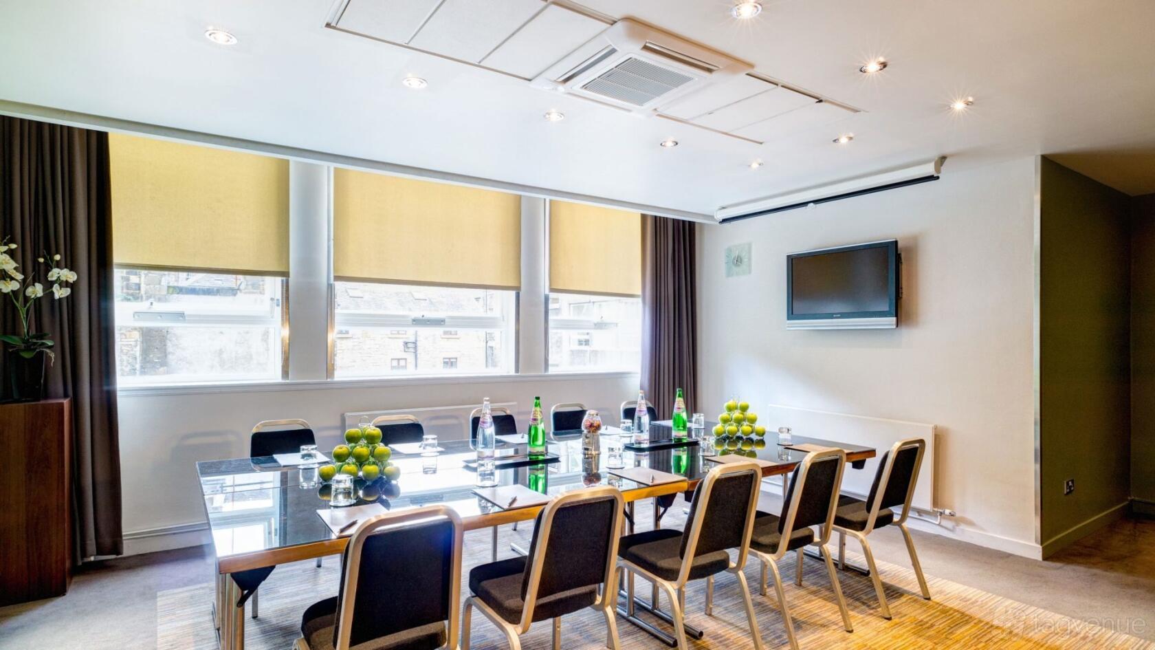 A meeting room with a glass conference table, black chairs, and floor-to-ceiling windows at Apex Grassmarket Hotel.