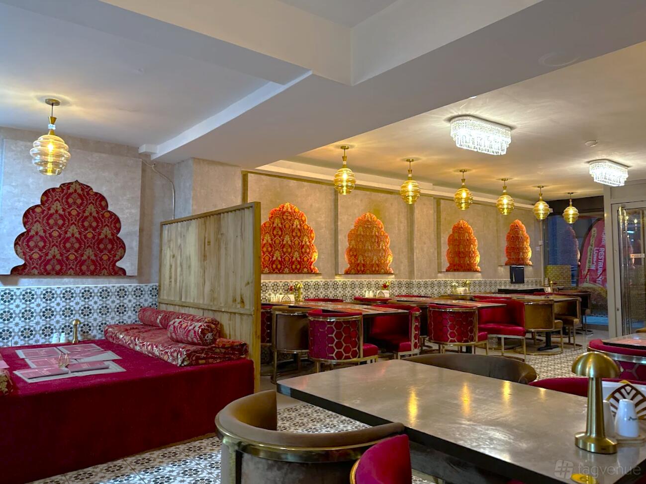 A restaurant with patterned tile walls, red cushioned seating, and gold pendant lighting at Monal Restaurant London.