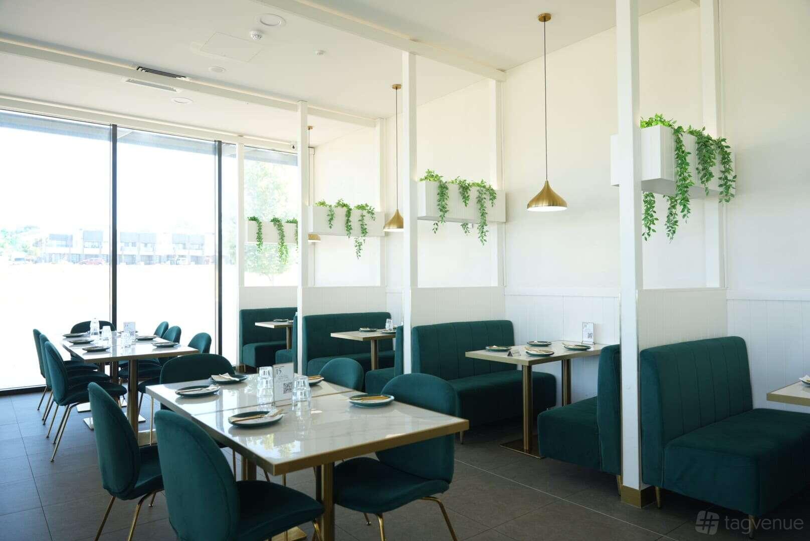 A dining room with green velvet booths, white marble tables, and hanging pendant lights at The Mustard Seed - Mount Barker.