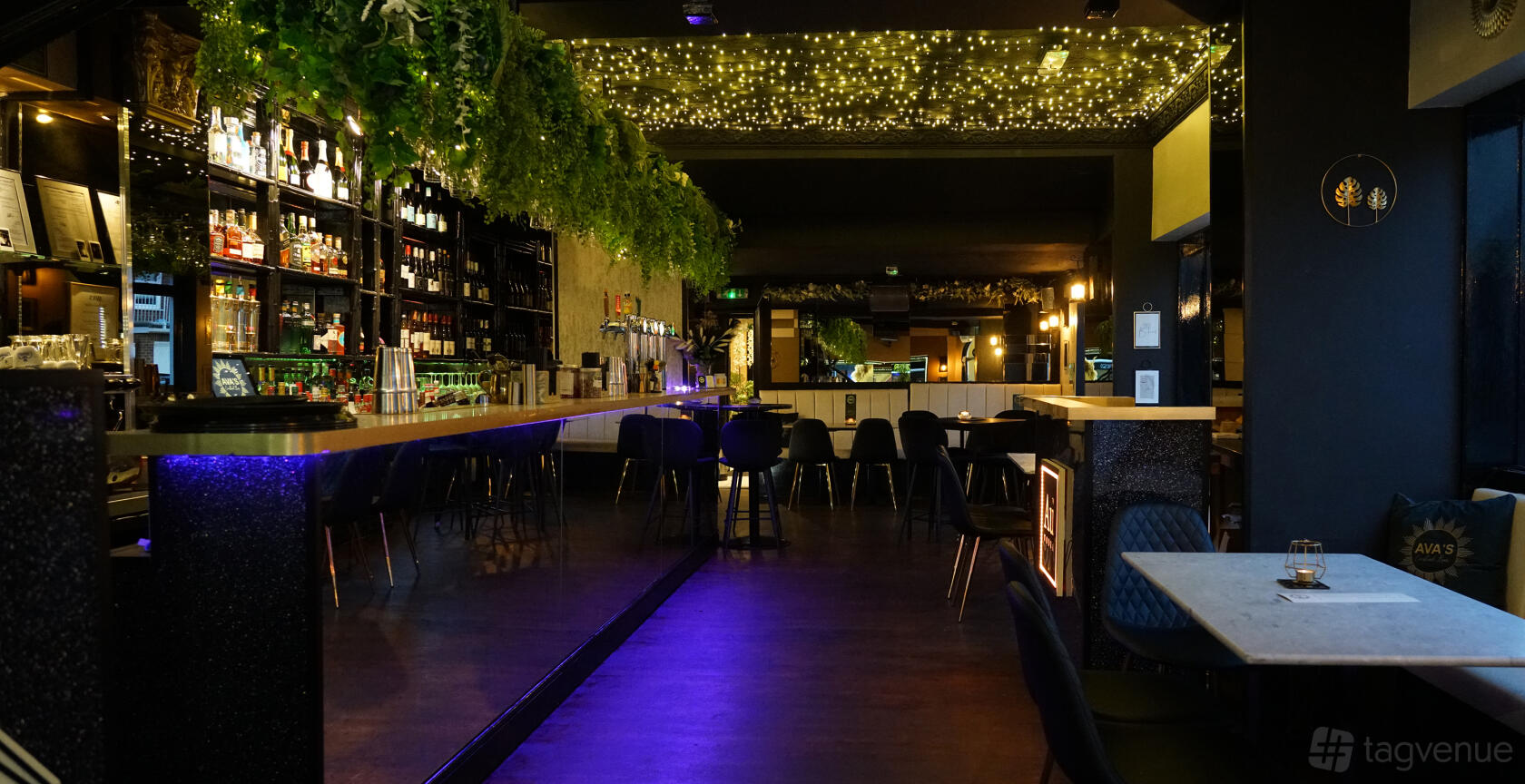 A function room with a long mirrored bar, hanging greenery, and a ceiling of fairy lights at Monarch Cocktail Bar.