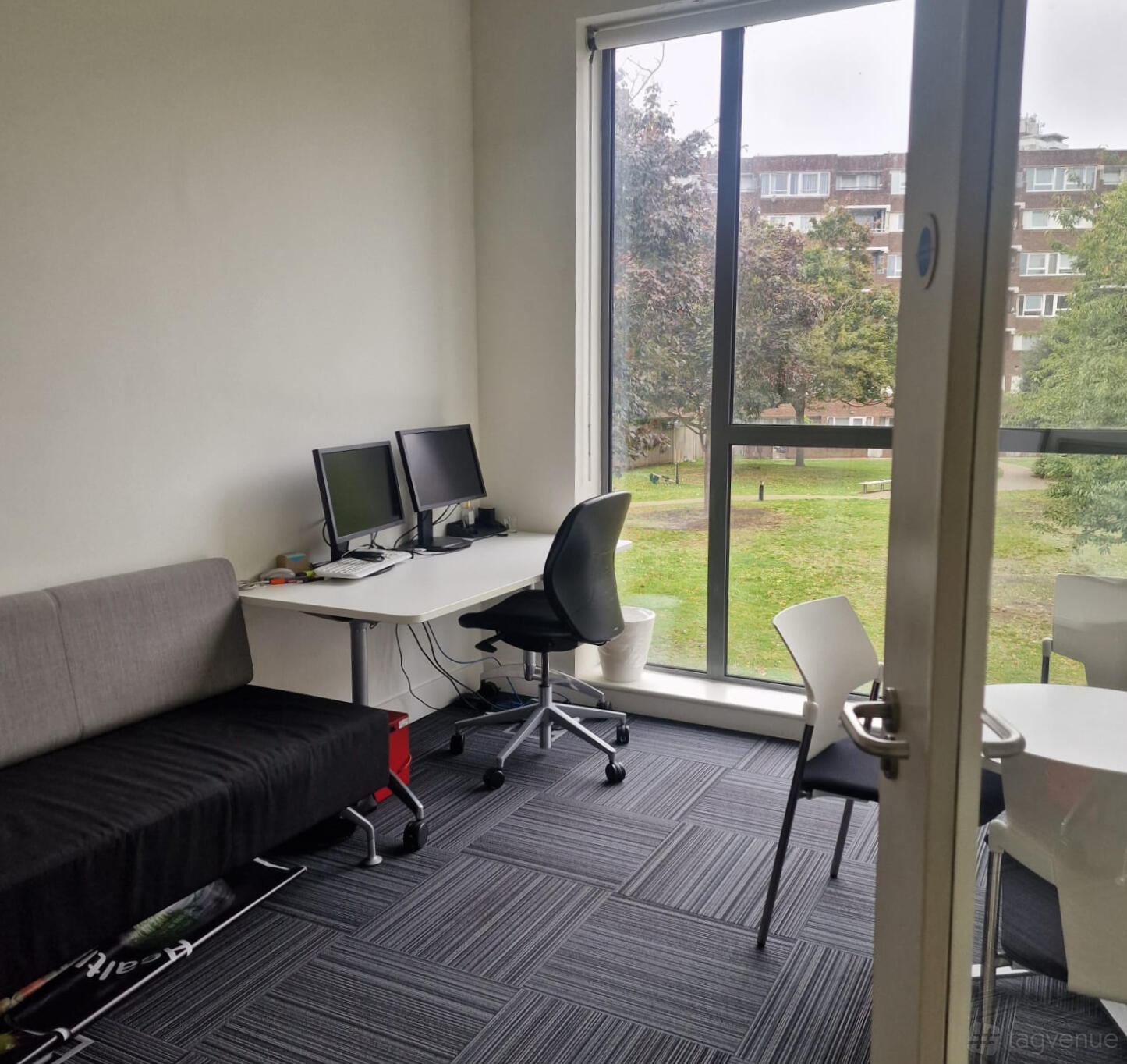 A meeting room with large windows, two computer monitors on a desk, and a gray sofa at St Pauls Way Community Centre.
