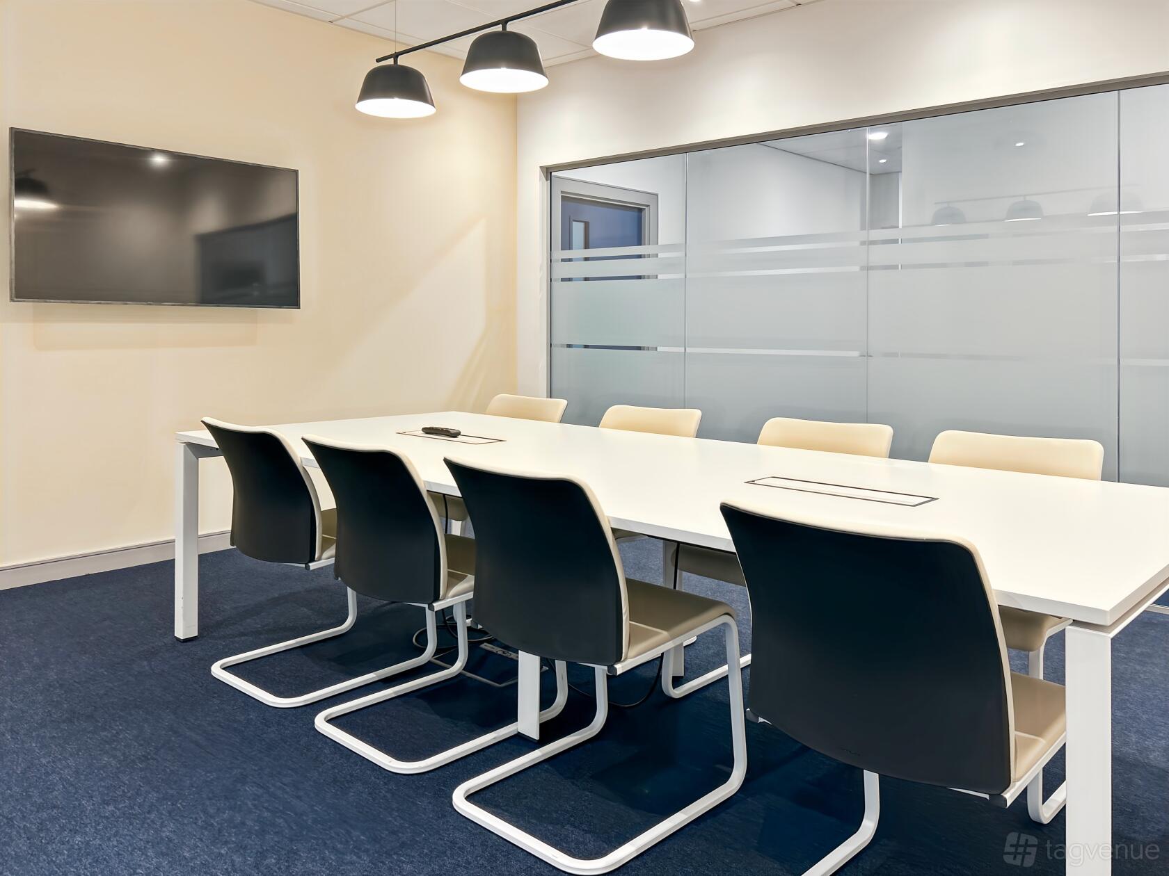 A boardroom with a long white conference table, black chairs, a wall-mounted screen, and frosted glass panels at Regus - Weavers Court.