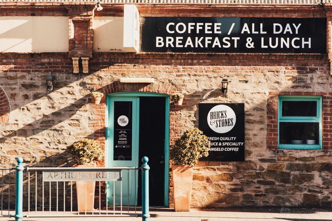 A café exterior with exposed brick walls, teal doors, and signage for breakfast and lunch at Bricks and Stones Cafe.