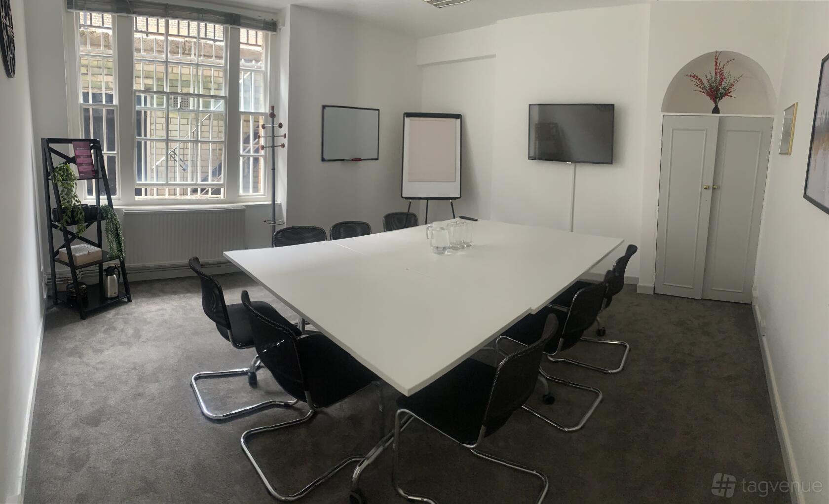 A meeting room with a long white table, black chairs, a flip chart, and a wall-mounted screen at Citibase London Victoria Catherine Place.
